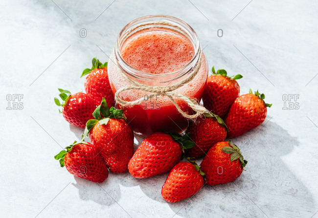 Composition with fresh homemade strawberry juice in glass jar wrapped with twine placed on marble surface with whole berries