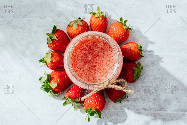Composition with fresh homemade strawberry juice in glass jar wrapped with twine placed on marble surface with whole berries