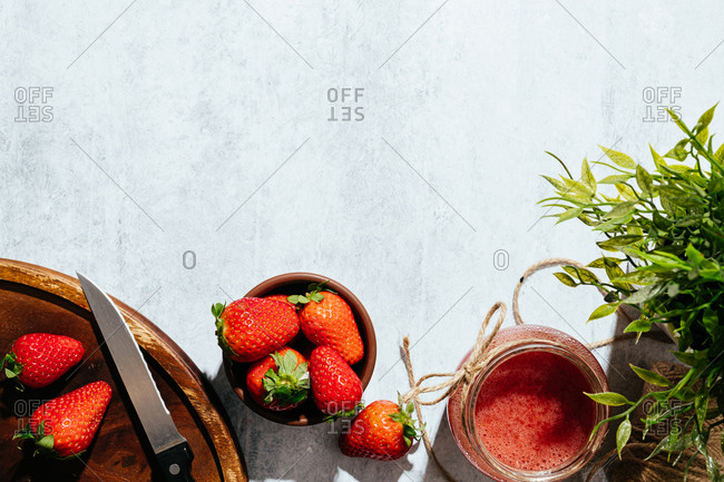 Composition with fresh homemade strawberry juice in glass jar wrapped with twine placed on marble surface with whole berries and knife