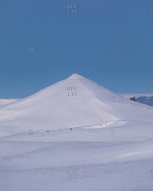 Minimalist winter landscape with snowy hill and valley under clear blue sky in sunny day in Iceland