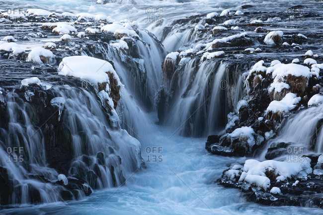 Amazing Nordic scenery of frozen waterfalls and river flowing through rough volcanic terrain covered with snow in Iceland
