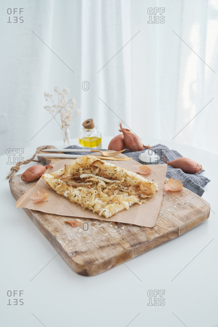 From above delectable puff pastry with onion and cream cheese placed on rustic cutting board on table near cooking ingredient at home