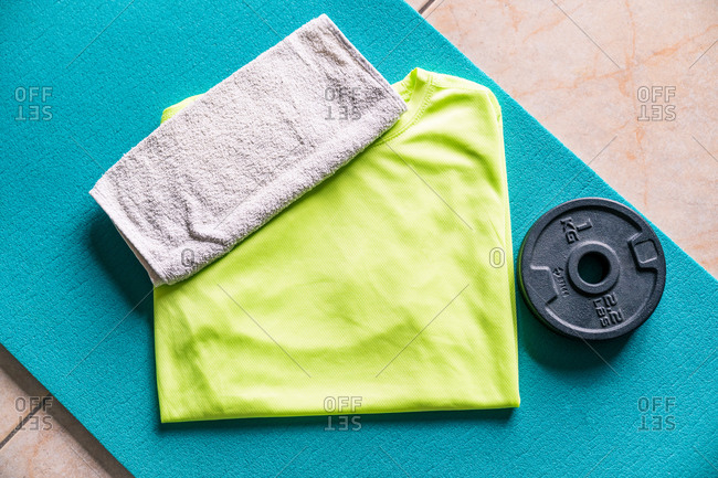 From above sports set for sportsman consisting of towel on vibrant green active wear in composition with turquoise sports mat and black round weight prepared for comforting training in contemporary fitness center