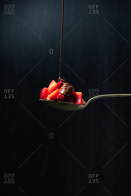 Delicious chocolate ganache jet of chocolate falling on top of a strawberry perched on a spoon