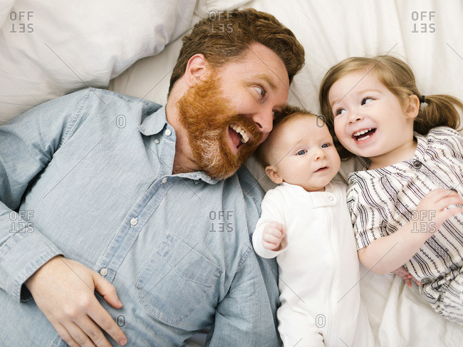 Father and children (2-3 months, 2-3) lying on bed and laughing