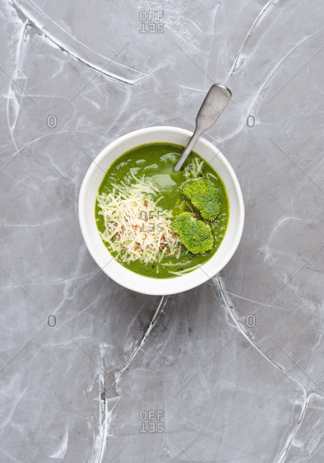 Overhead view of bowl with green broccoli cream soup served with ground cheese parmesan and linen seeds