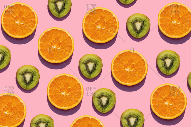 Pattern of orange and kiwi fruit slices against pink background