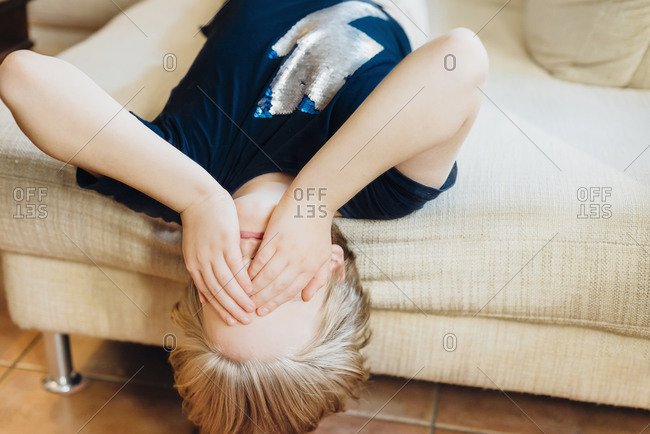 Boy lying on couch covering his eyes