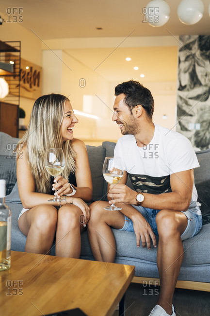 Laughing couple sitting on the couch with glasses of white wine