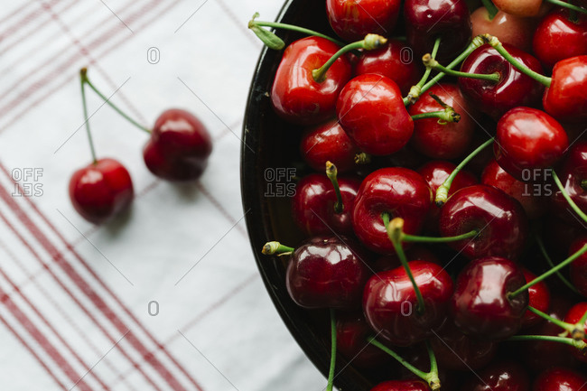 Overhead view of fresh cherries in a ceramic bowl on a red striped napkin