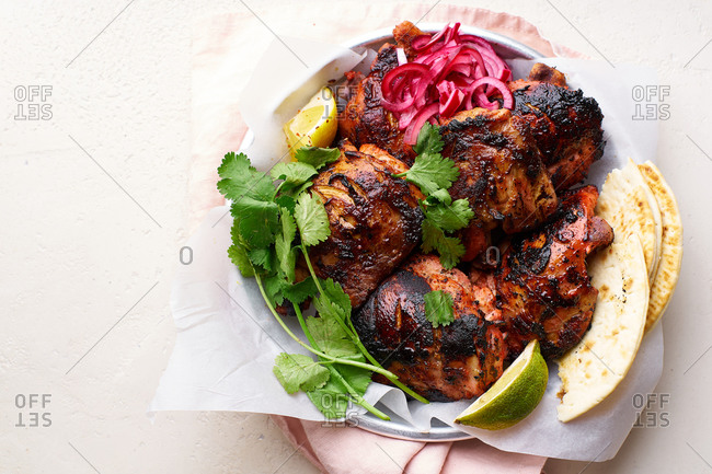 Overhead image of tandoori chicken thighs marinated in tikka sauce, grilled and served with mint chutney, lime and cilantro. Traditional indian cuisine starter.