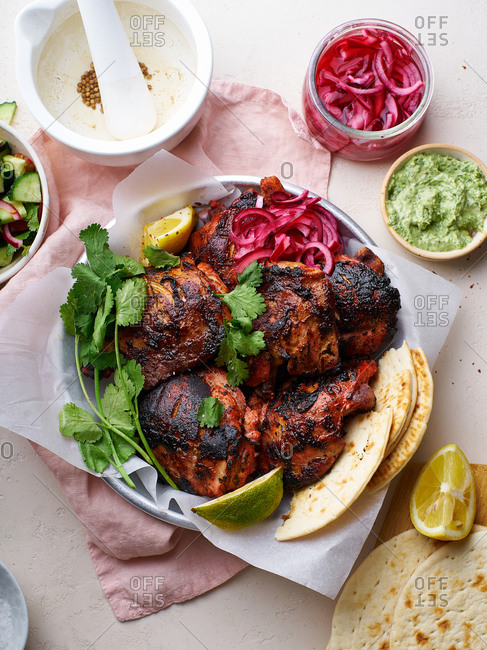 Overhead image of tandoori chicken thighs marinated in tikka sauce, grilled and served with mint chutney, lime and cilantro. Traditional indian cuisine starter.