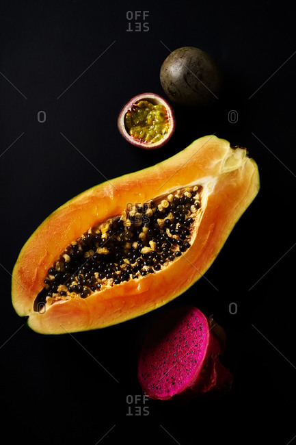 Still life with sliced papaya, pitaya and passion fruit on black background