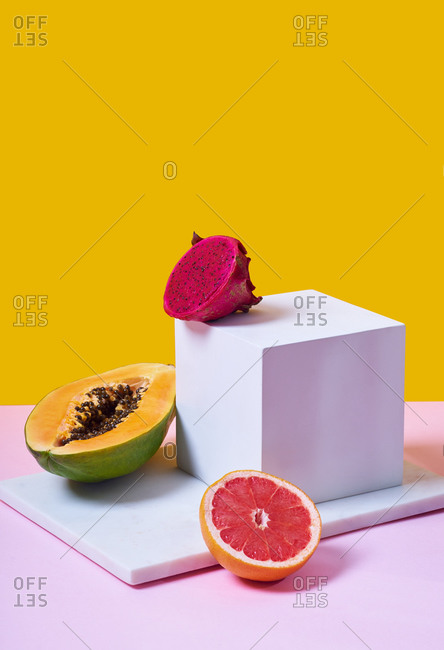 Still life with tropical fruits, glass of orange juice and white cube on colorful background