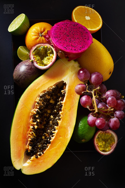Still life with sliced papaya, grapes, pitaya and tropical fruits on black background