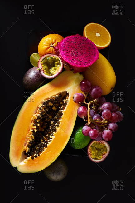 Still life with sliced papaya, grapes, pitaya and tropical fruits on black background
