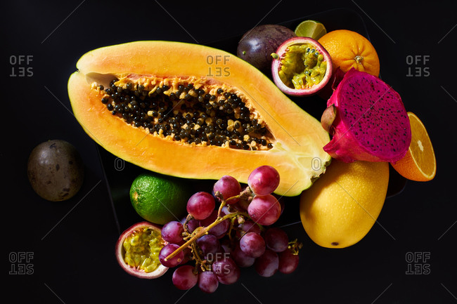 Still life with sliced papaya, grapes, pitaya and tropical fruits on black background