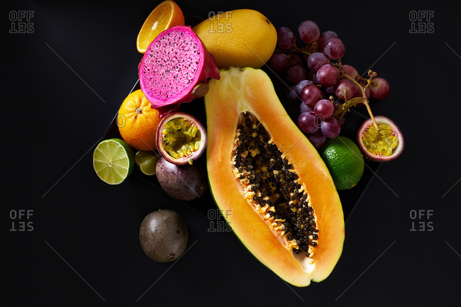 Still life with sliced papaya, grapes, pitaya and tropical fruits on black background