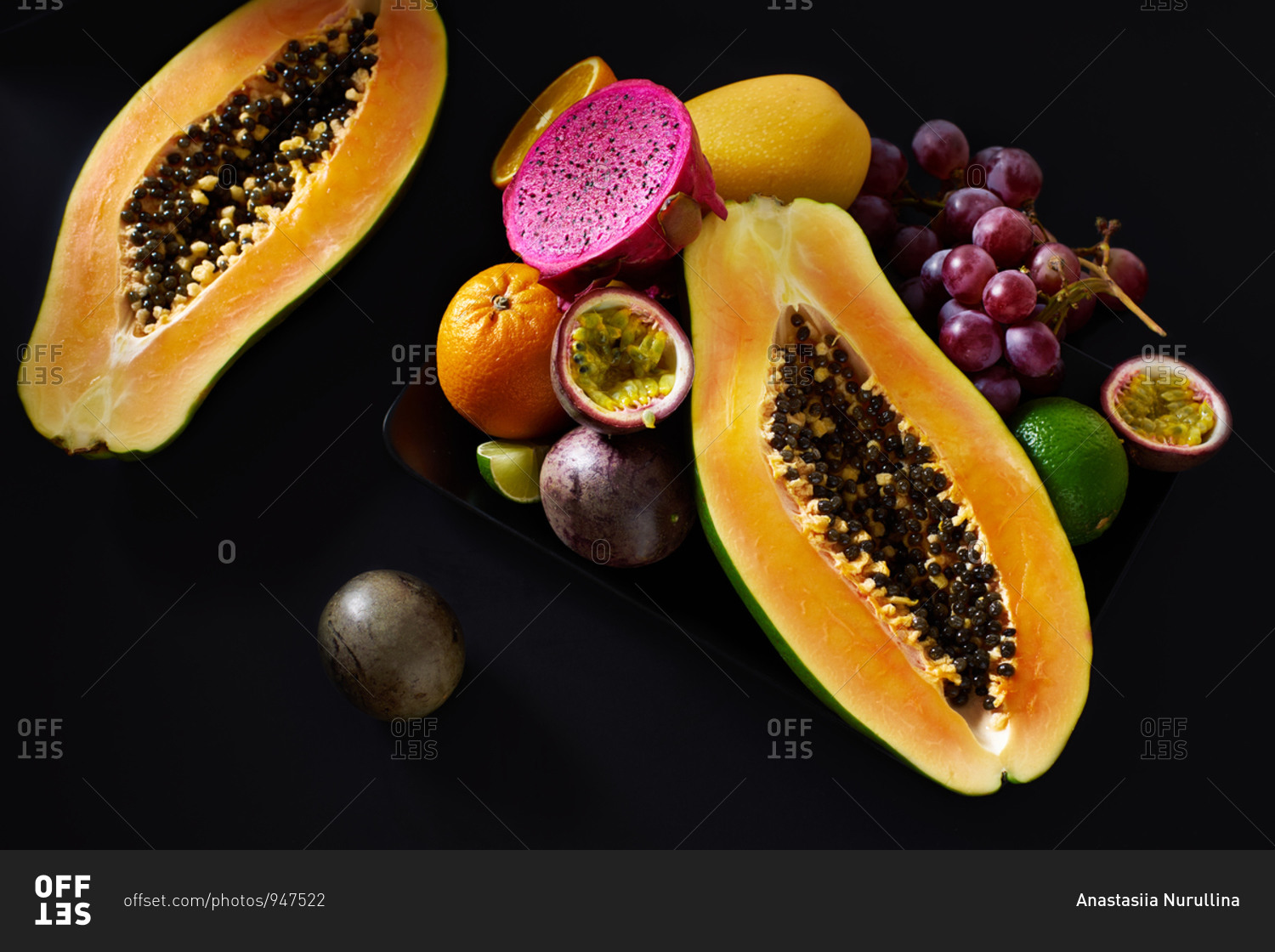 Still life with sliced papaya, grapes, pitaya and tropical fruits on black background