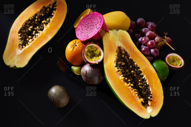 Still life with sliced papaya, grapes, pitaya and tropical fruits on black background