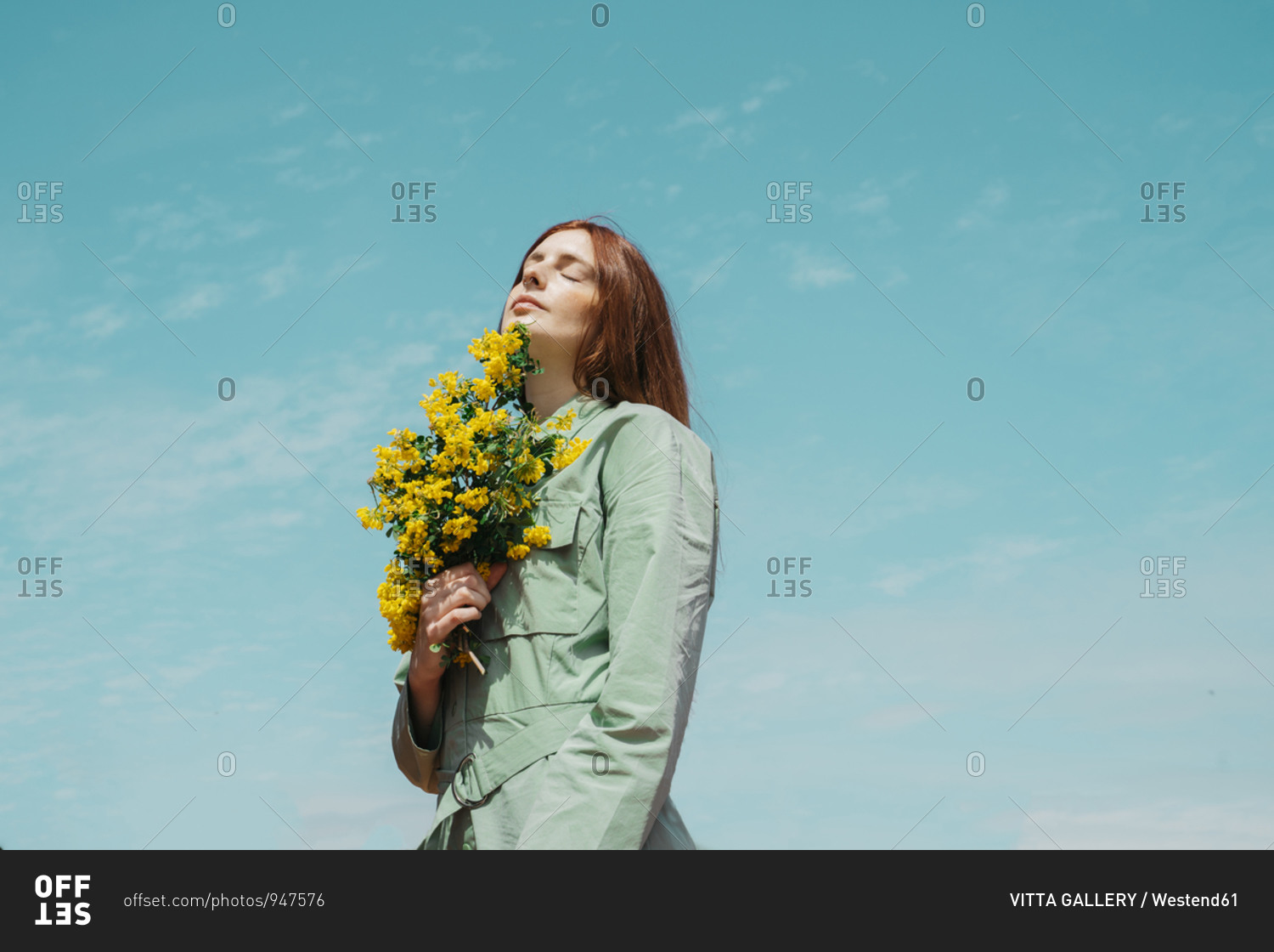 Portrait of redheaded young woman with eyes closed standing against sky holding bunch of yellow flowers