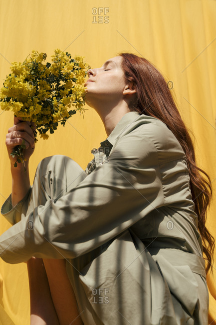 Portrait of redheaded woman with eyes closed holding bunch of yellow flowers against yellow background