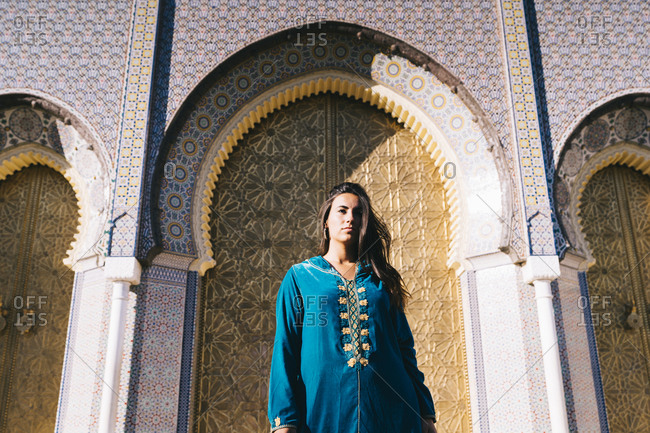 Young woman standing in front of traditional acritude wearing Moroccan robe- Morocco