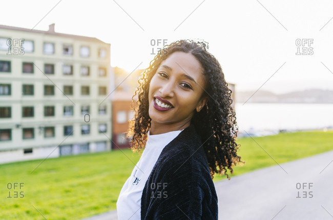 Portrait of smiling young woman with ringlets at backlight