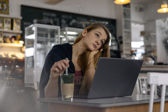 Daydreaming young woman with laptop in a cafe