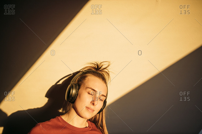 Portrait of young woman with headphones in sunshine at home