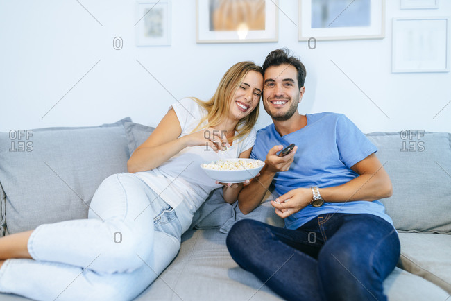 Smiling couple watching TV while enjoying popcorn on sofa at home