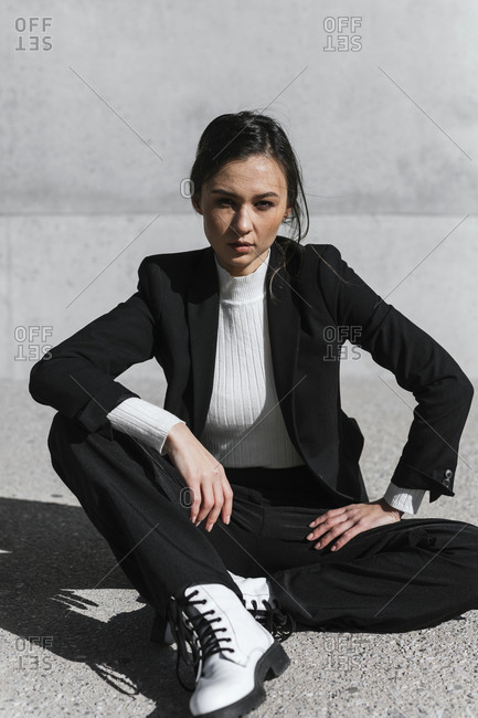 Young woman wearing black suit sitting on floor in front of concrete wall
