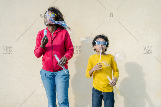 African-American mother and son dressed in colorful casual clothes playing and making soap bubbles outside