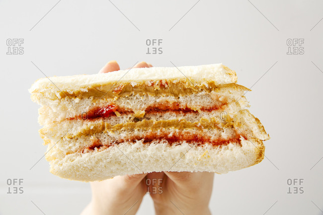 Hands holding a peanut butter and strawberry jelly sandwich in front of white background