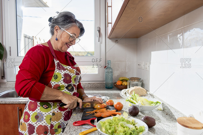 Smiling old lady cutting vegetables in the kitchen.