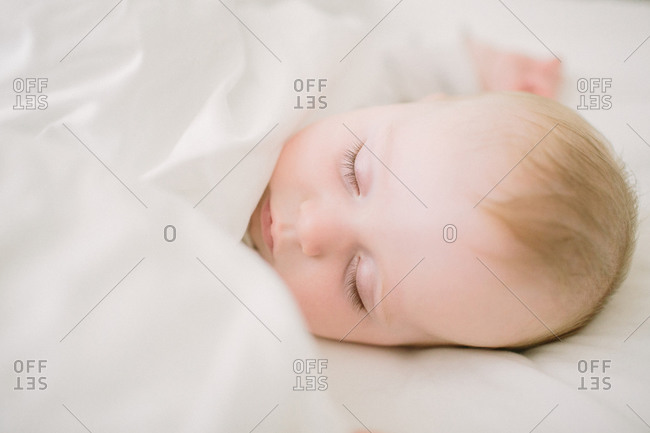 Peaceful and ethereal sleeping baby surrounded in white blanket
