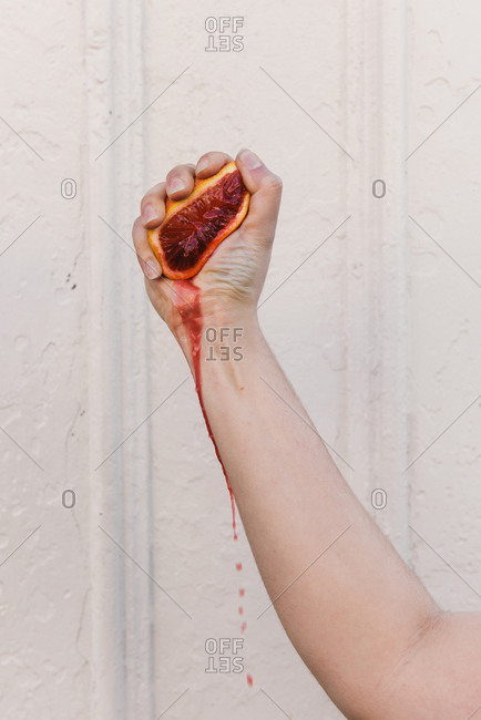 Woman's hand squeezing the juice out of a blood orange and dripping