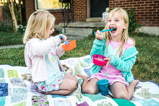 Two girls eating ice cream on a blanket outdoors