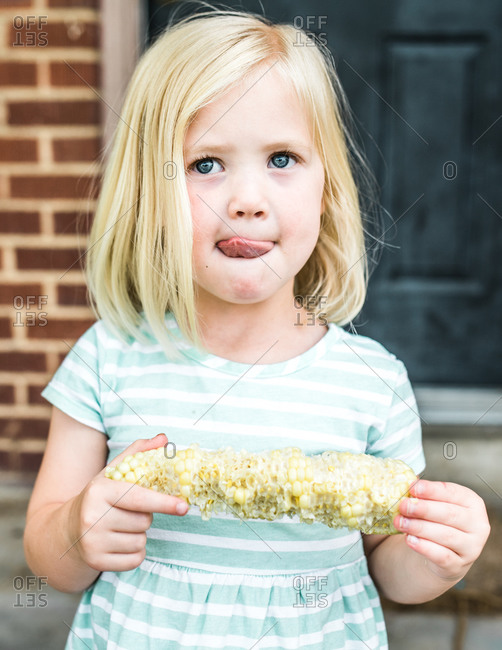 Blonde girl eating corn on the cob outside