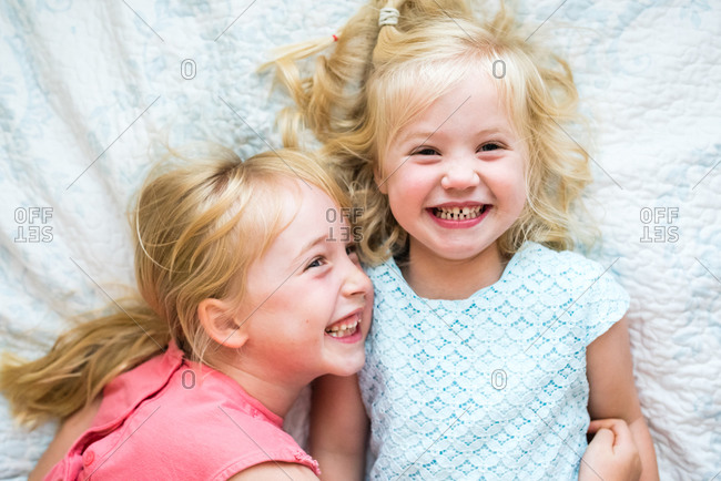 Portrait of two little blonde girls lying on white blanket