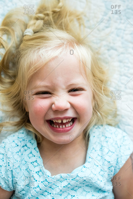 Portrait of a little blonde girl lying on white blanket and laughing