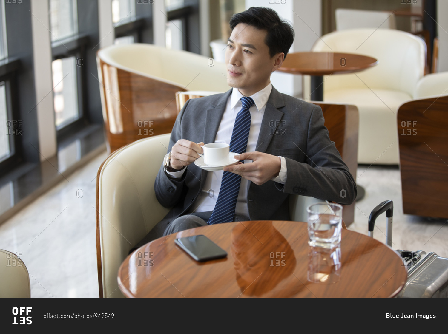 Confident Chinese businessman drinking coffee in airport lounge