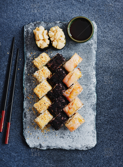 Minimalistic flatlay composition with sushi rolls, chopsticks and soy sauce on dark blue background