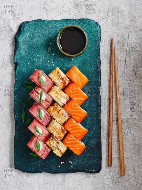 Japanese maki sushi rolls with salmon, tuna and smoked eel with chopsticks served on turquoise stone serving board on light background