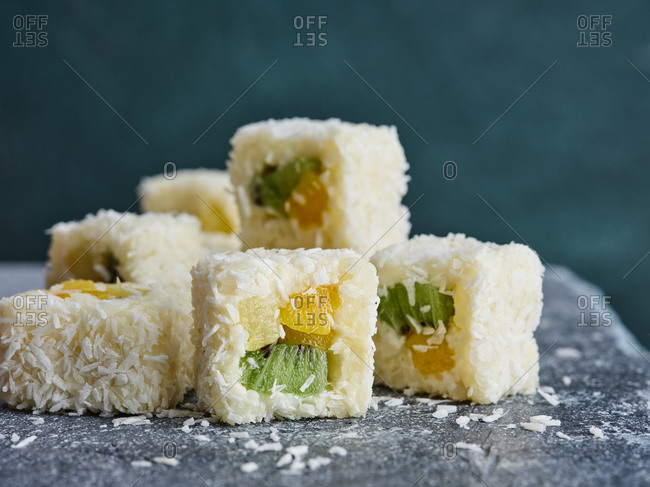 Close up view of sweet sushi rolls with shredded coconut and tropical fruits (mango, pineapple and kiwi fruit)
