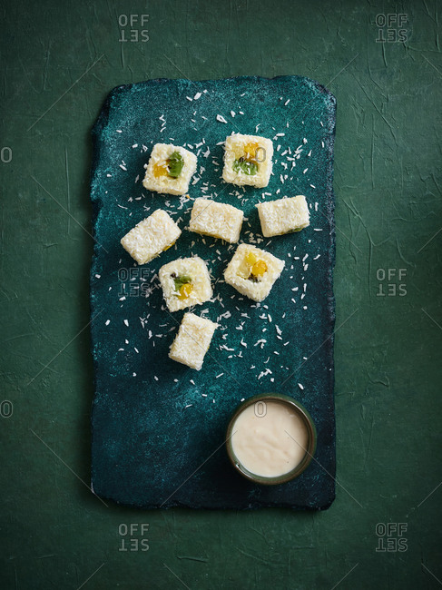 Flatlay of dessert sushi rolls with fresh tropical fruits and coconut sauce on turquoise stone serving board