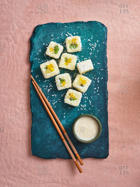 Dessert sticky rice sushi with tropical fruits and coconut sauce served on turquoise stone platter on pink background