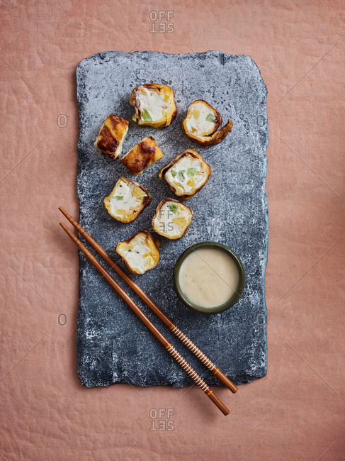 Top angle view of sweet dessert sushi rolls with tropical fruits and delicious coconut dipping sauce on pink background