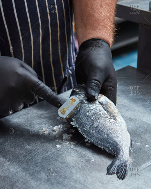 The hands of men clean raw fish scales on a metal surface. The process of cooking food in the restaurant