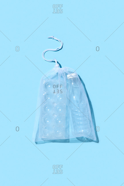 Transparent reusable shopping bag with plastic eggs container and bottle on a light blue background with shadow, copy space. Flat lay. Eco friendly concept.